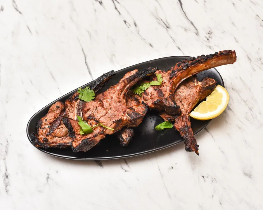 Charcoal-grilled lamb chops with fresh coriander and lemon on a black platter